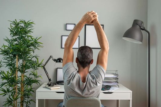Man stretching arms up behind head at desk while working.